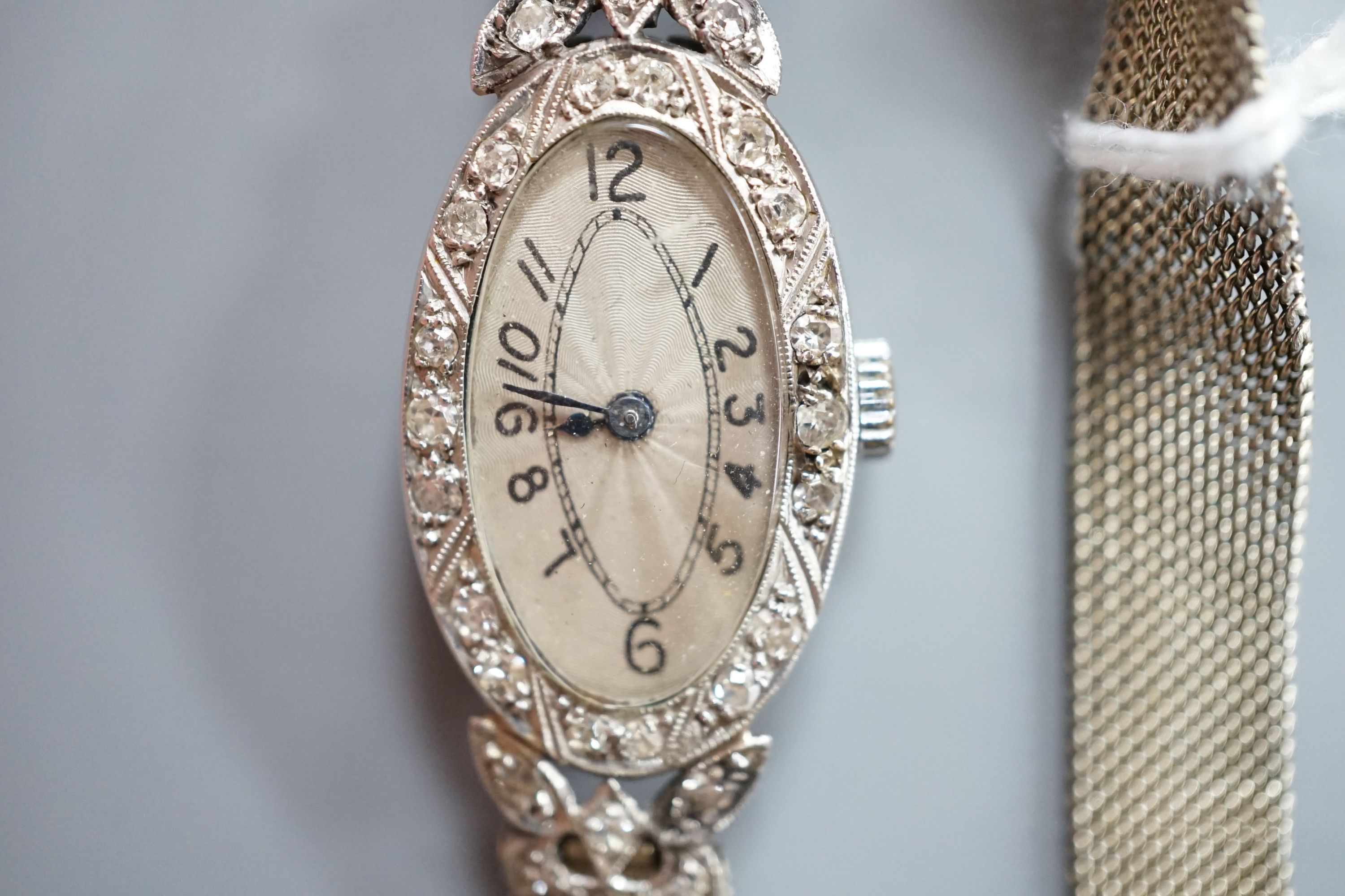 A lady's mid 20th century white metal (stamped platinum) and diamond set manual wind oval cocktail watch, on a white metal mesh bracelet stamped '18', gross weight 21.6 grams.